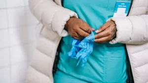 Pflegekraft zieht Einmalhandschuhe an, bevor sie die Versorgung übernimmt