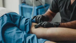 Pflegekraft mit Handschuhen versorgt das Bein eines liegenden Patienten