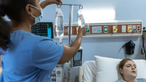 Pflegefachkraft kontrolliert die Infusion am Bett einer liegenden Patientin