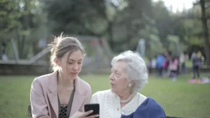 Tochter nutzt eine Pflege-App auf dem Smartphone neben ihrer älteren Mutter