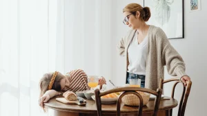 Erschöpfte Frau sitzt neben ihrer pflegebedürftigen Mutter in der Küche